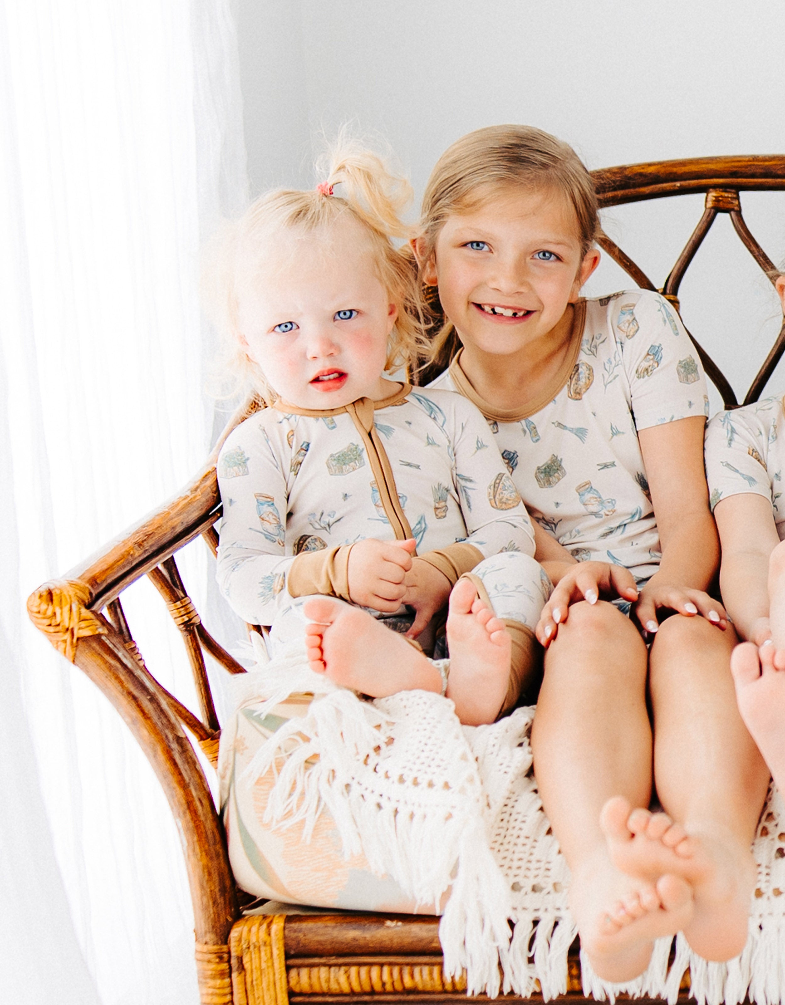 little girl with her sister sitting on a chair with Meadow Lane Kids Heirloom Homestead soft TENCEL toddler pajamas on